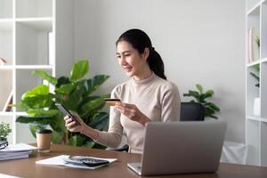 contento joven asiático mujer participación crédito tarjeta utilizando móvil pago a hogar. sonriente hembra cliente compras haciendo compra en teléfono inteligente recepción efectivo espalda concepto foto