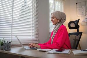 Muslim business woman hijab working about financial with business report and calculator on laptop in home office photo