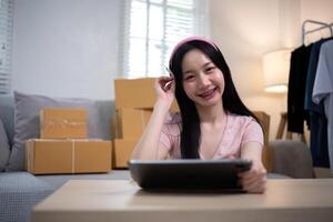 Asian woman small business entrepreneur working from home use tablet for commercial inspection. online marketing Packaging box, concept ecommerce photo