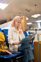 contento joven mujer asiático es sentado en aeropuerto cerca maleta y leyendo mapa foto