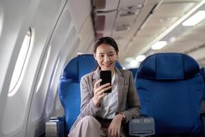 Asian young businesswoman successful or female entrepreneur in formal suit in a plane sit in a business class seat and uses a smartphone during flight. Traveling and Business concept photo