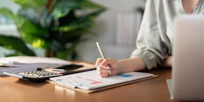 Asian Businesswoman using laptop computer and working at home with calculator document on desk, doing planning analyzing the financial report, business plan investment, finance analysis concept photo