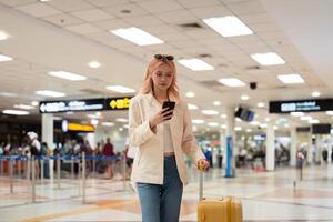 un mujer asiático caminando en un aeropuerto. móvil, maleta y viaje con un joven hembra en un internacional viaje para trabajo o viaje foto