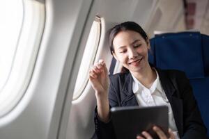 Smiling happy business woman asian flying and working in an airplane in first class, Woman sitting inside an airplane using digital tablet photo