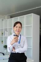 Young successful employee business woman hold craft paper cup coffee stand at desk with laptop pc computer at office. Achievement career concept photo