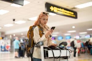 un mujer asiático caminando en un aeropuerto. móvil, maleta y viaje con un joven hembra en un internacional viaje para trabajo o viaje foto