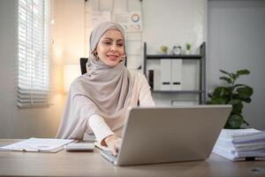 asiático musulmán mujer de negocios en hijab cabeza bufanda trabajando con papel documento en el moderno oficina. diversidad y oficina concepto foto