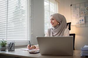 asiático musulmán mujer de negocios en hijab cabeza bufanda trabajando con papel documento en el moderno oficina. diversidad y oficina concepto foto