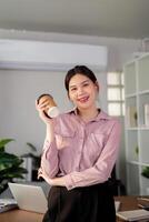 Young successful employee business woman hold takeaway craft paper cup coffee at desk at office. Achievement career concept photo