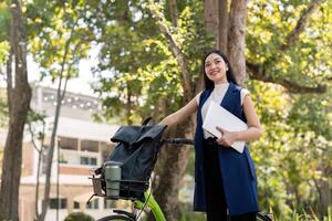 Asian businesswoman with bicycle holding a laptop and outside the office building. Woman commuting on bike go to work. Eco friendly vehicle, sustainable lifestyle concept photo