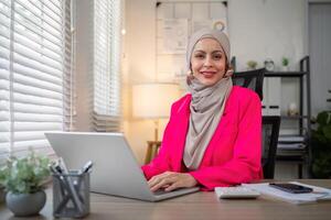 Muslim business woman hijab working about financial with business report and calculator on laptop in home office photo