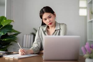 Asian Businesswoman using laptop computer and working at home with calculator document on desk, doing planning analyzing the financial report, business plan investment, finance analysis concept photo