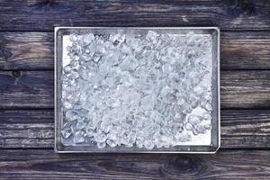 Crushed ice on tray on wooden background. Copy space, top view photo