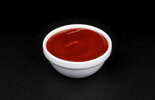 Ketchup in white bowl on black background photo