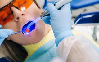 A young beautiful girl in dental glasses treats her teeth at the dentist with ultraviolet light. filling of teeth photo