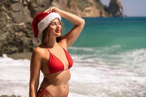 A woman in Santa hat on the seashore, dressed in a red swimsuit. New Year's celebration in a hot country. photo