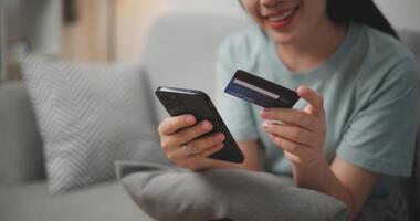 Selective focus, Hands of Young asian woman sitting on sofa holding credit card making online payment for purchase in web store using smartphone. photo