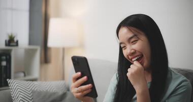 Selective focus, Happy young woman sitting on sofa looking at smartphone feel surprised while online shopping in living room at home photo