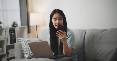 Selective focus ,Happy young woman sitting on sofa using laptop and mobile phone for online shopping in living room at home, Technology money wallet and Online payment concept photo
