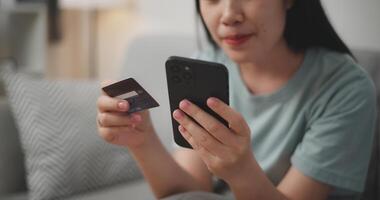 Selective focus, Hands of Young asian woman sitting on sofa holding credit card making online payment for purchase in web store using smartphone. photo