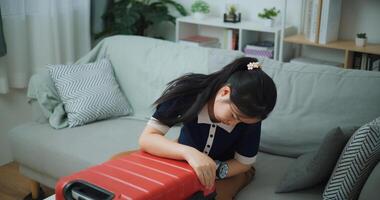 High angle view of Asian teenager woman sitting on sofa is closing a packed suitcase in the living room, Preparation travel suitcase at home. photo
