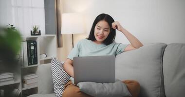 selectivo enfocar, relajado joven mujer sentado en sofá utilizando ordenador portátil para en línea compras sin efectivo en vivo habitación a hogar ,Internet conectividad y en línea concepto. foto