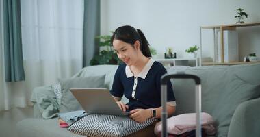 Portrait of Asian teenager woman sitting on sofa using laptop for prepare booking hotel and airplane ticket for travel. backpacker travel concept. photo