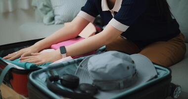 Selective focus hands of Asian teenager woman sitting on sofa packing travel luggage with clothes for traveling trip, Preparation travel suitcase at home. photo