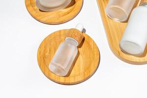 close up of face beauty serum dropper bottle of matte glass and bamboo lid on wooden tray on white background. Skin care package photo