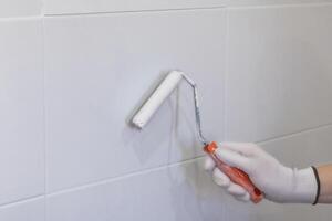Painting tiles in the kitchen in the bathroom, white paint with a roller. Hand in glove with roller photo