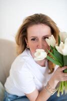 mujer participación blanco tulipanes cerca a rostro. casual atuendo. de la madre día y De las mujeres día concepto foto