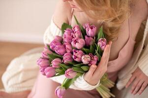 mujer participación un ramo de flores de púrpura tulipanes, acogedor de punto suéter detalle foto