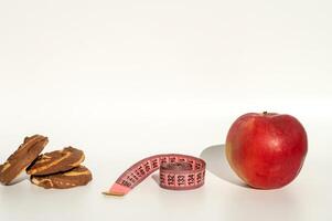 Measuring tape with cute emoji face on white background, apple and chocolate cookie shadow play photo