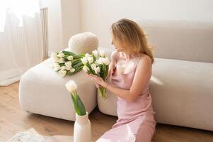 Woman in pink dress holding white tulips on beige couch. photo