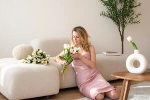 Woman in pink dress holding white tulips on beige couch. photo
