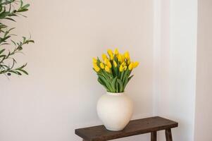 Yellow tulips in a white vase on a wooden bench. photo