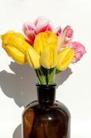 Yellow and pink tulips in brown glass bottle on white background. photo