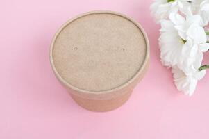 Brown cardboard food container with lid on a pink background with white flowers. photo