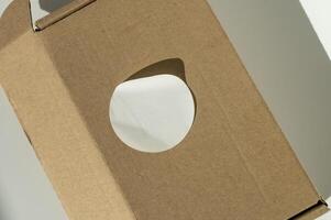 Brown cardboard box with circular white sticker on a neutral background. photo