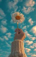 AI generated A hand lifts a single flower towards a vibrant blue sky dotted with clouds photo