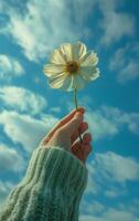 AI generated A hand lifts a single flower towards a vibrant blue sky dotted with clouds photo