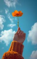 AI generated A hand lifts a single flower towards a vibrant blue sky dotted with clouds photo