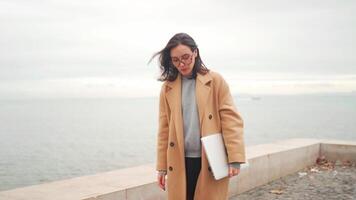 a woman in a coat and glasses walking on the beach video