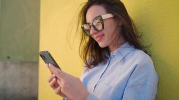 een vrouw in bril is leunend Aan een muur en gebruik makend van haar telefoon Aan een straat video