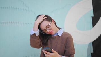 a woman in a sweater and jeans is looking at her phone while walking in front of a colorful wall video