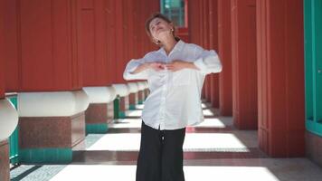 a woman in a white shirt is standing in an open area and posing to the camera video