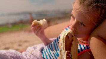 un' poco ragazza mangiare un' Banana su il spiaggia video