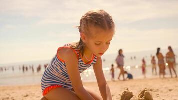 a little girl in a striped swimsuit is playing with sand in the beach video