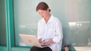 a woman sitting on the side walk with a laptop video