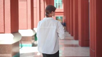 un confidente mujer en un blanco camisa participación un libro caminando video